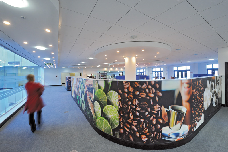 Female DVLA staff member in red coat, walking towards DVLA A2 cafe.