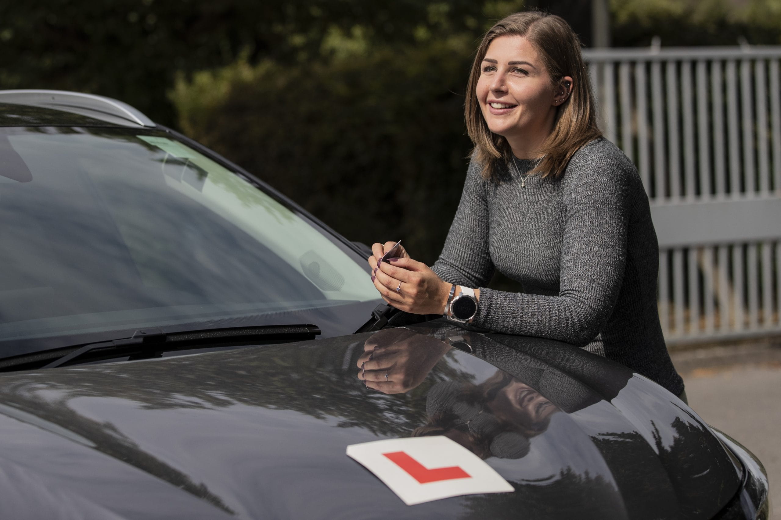 A young female standing alongside a black, L-plated car.