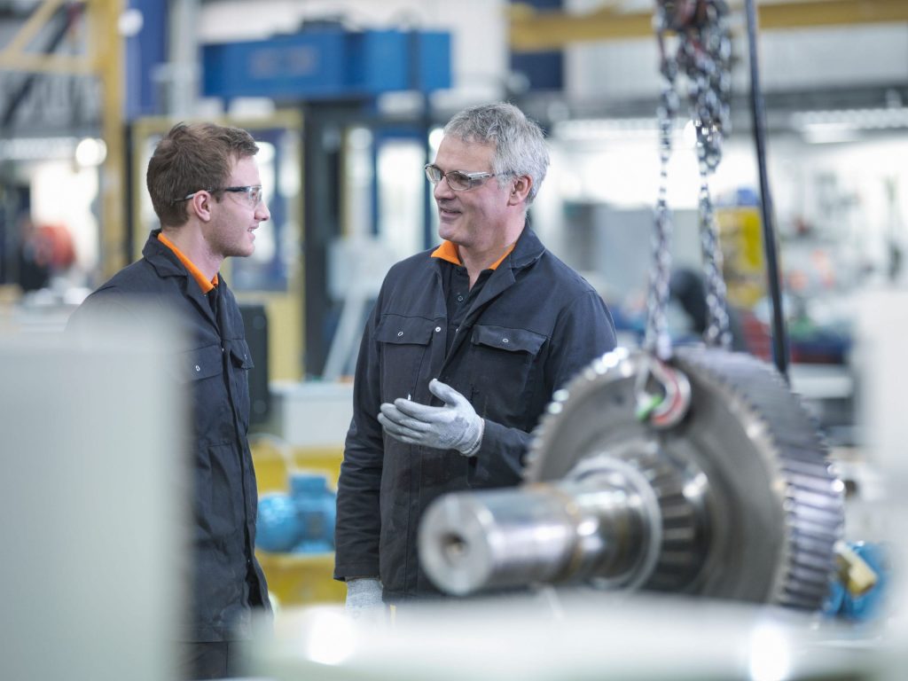 MCA engineer and apprentice in discussion next to gear wheel.