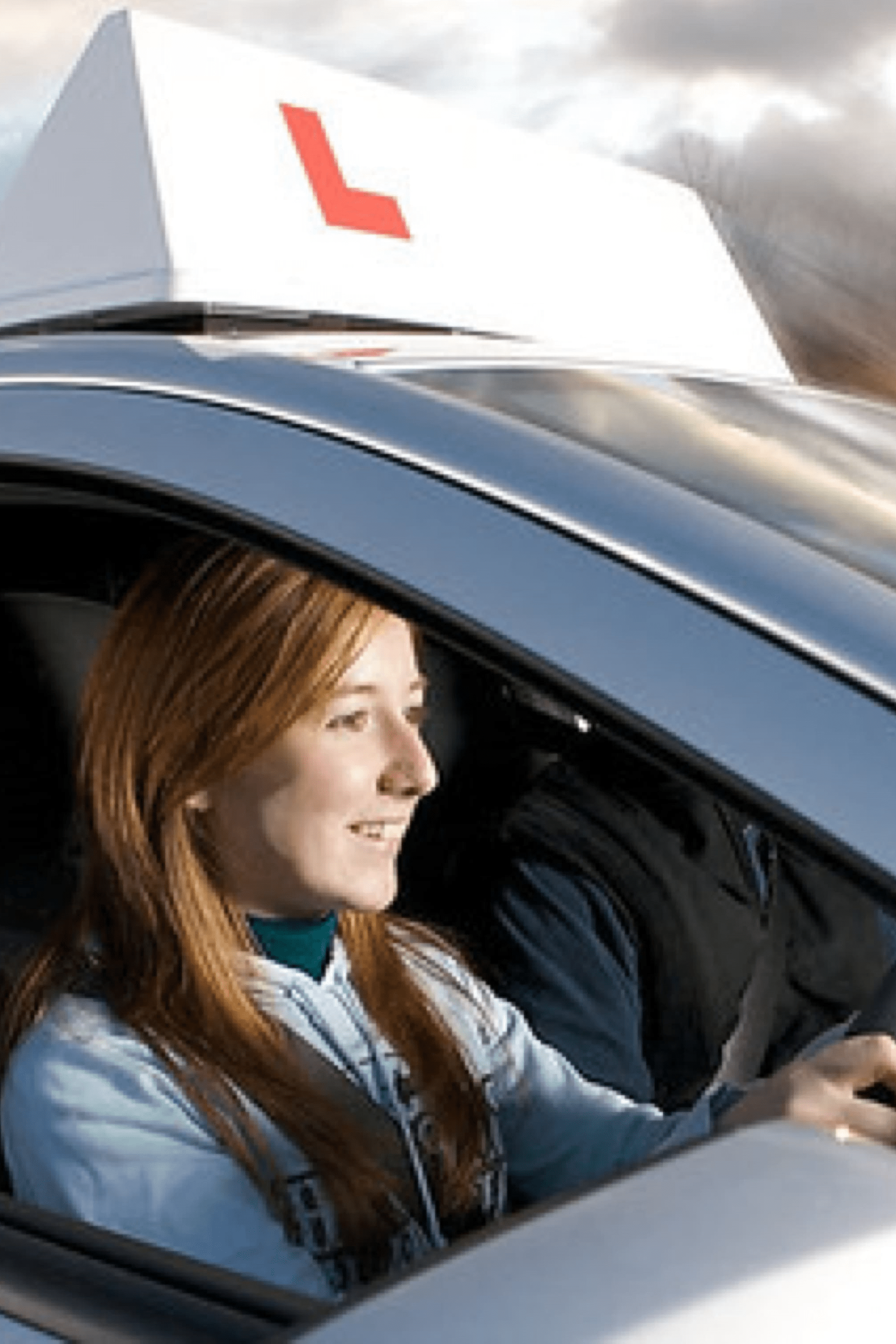 Young woman driving a car with a learner driver sign on the car roof.